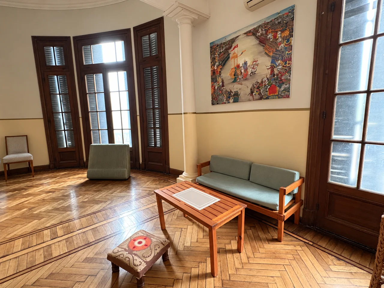 Salón de Gaiatri con sillón, mesa de madera, ventanales y piso de parquet